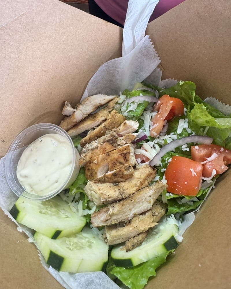 Sliced grilled chicken over salad with a pot of dressing